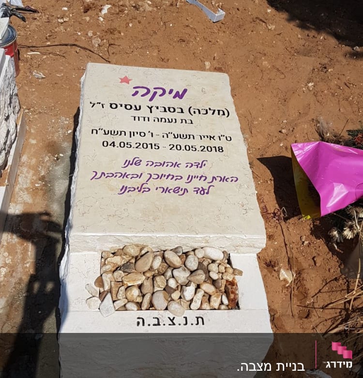 מצבה עם כיתוב בעברית ואבנים קטנות מונחות עליה